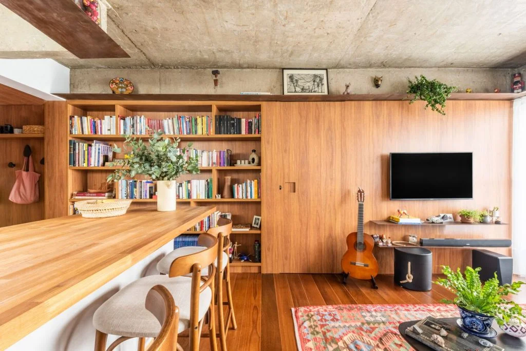 Sala de estar, biblioteca da família e balcão dividem o mesmo ambiente assinado por LCAC Arquitetura